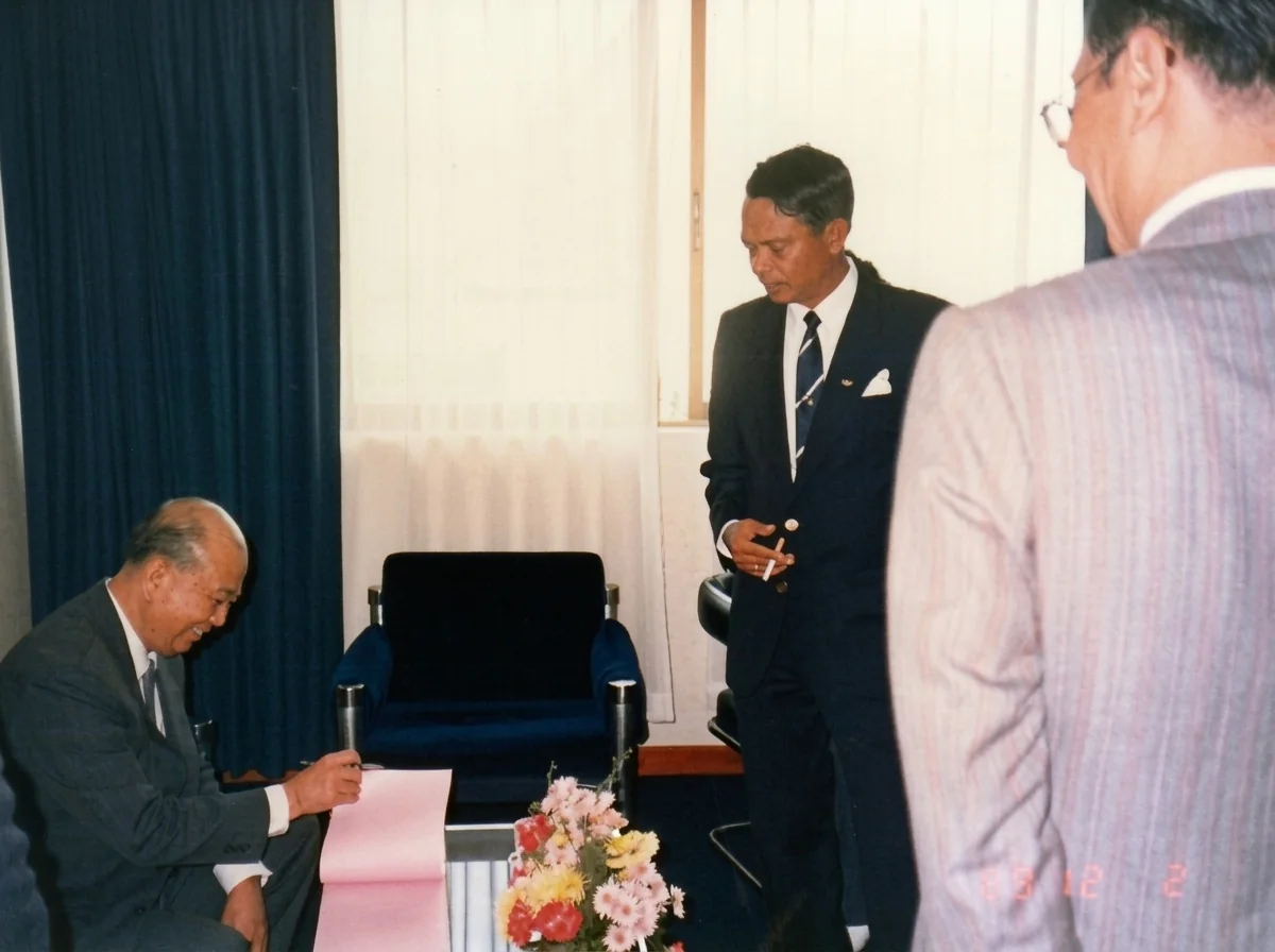 1989年12月2日合艾和平大典后，马共中央总书记陈平（左）在纪念册上签名留念，中为泰方吉迪将军，右为与会嘉宾