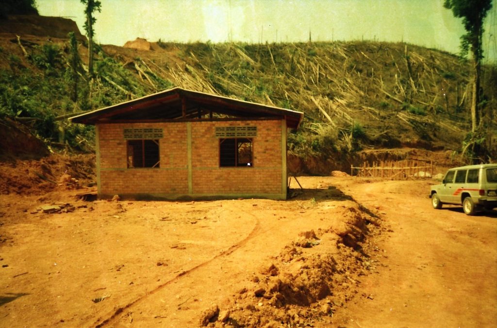1991年初和平村首批建成的红砖瓦房住宅：背靠刚垦殖完毕的山坡，门前辟出宽阔的红土村道，右侧停放着村委会越野吉普车。