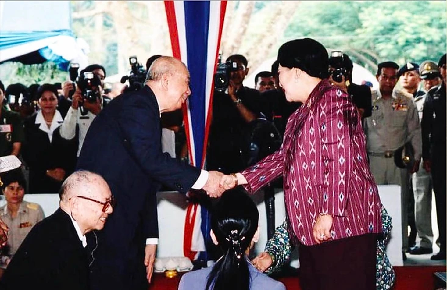 2005年9月15日，马共中央总书记陈平（左立者）与党主席阿都拉·西迪（左下）在泰南和平村向莅临视察的诗丽吉王后（右）致敬握手，朱拉蓬公主（中背影者）随侍在侧，象征着几十年丛林硝烟彻底化为真正的和平与和解。