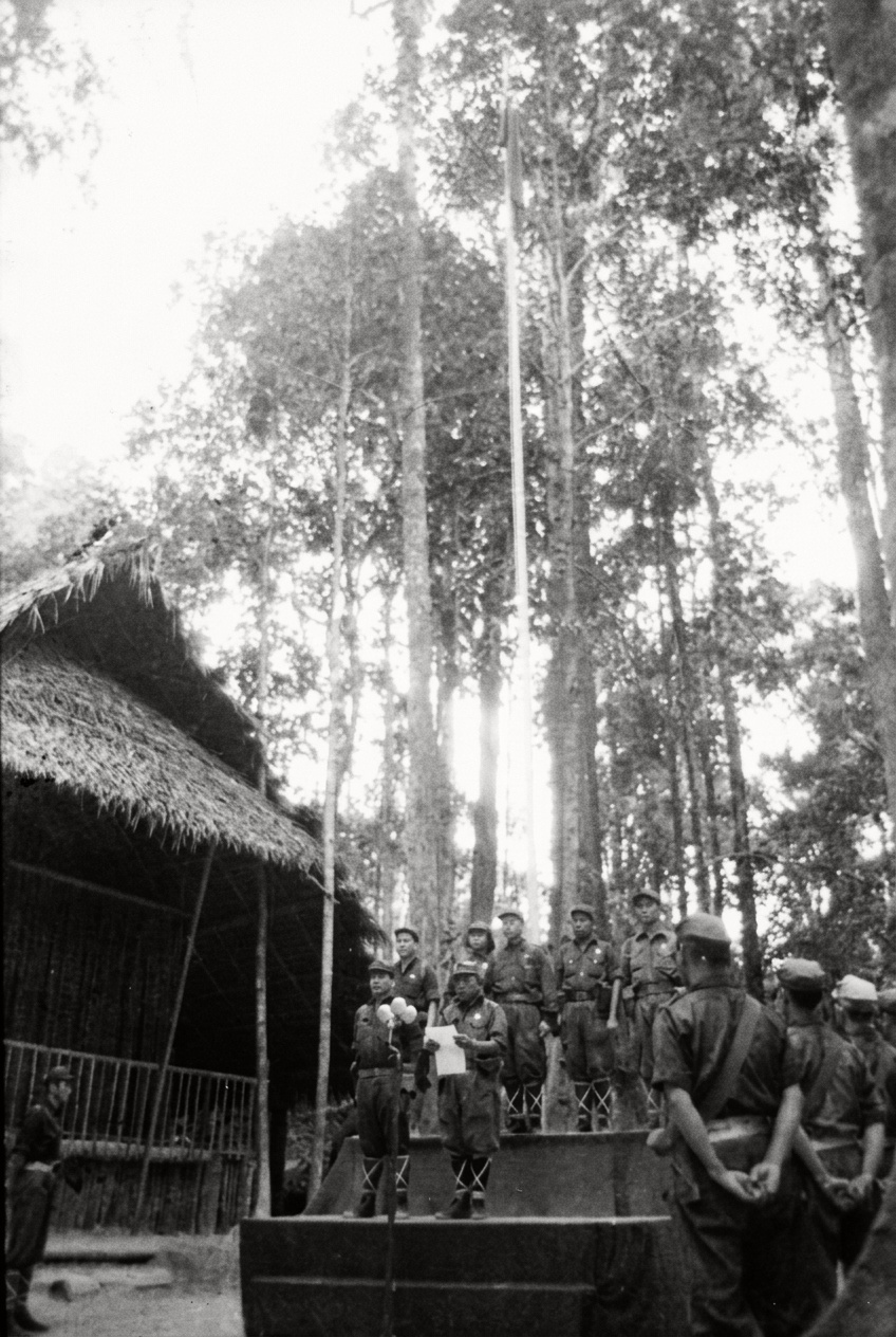 1968年6月20日密林营地高耸旗杆下的升旗仪式现场，部队指挥员向列队肃立的武装指战员发表讲话。