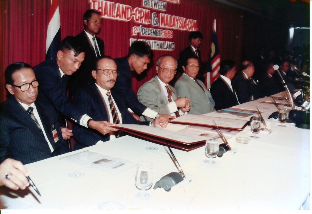 1989年12月2日《合艾和平协议》签署席长镜头：马来西亚政府、泰王国政府与马来亚共产党三方全权代表在长桌前同时签署协议文本，开启了体面和平与战后回归计划的历史新页。