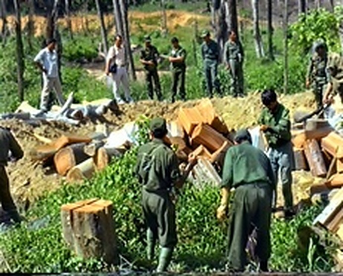 人民军指战员围立在原木桩旁，轮流将枪支构件砸毁变形，彻底解除武器的战斗功能。